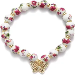 Porcelain floral bead stretch bracelet detail with gold charms and sparkling butterfly pendant.