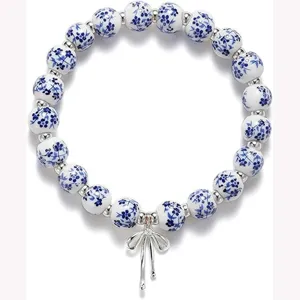 Blue and white ceramic floral bead bracelet with silver bow pendant, elegant elastic wristband.