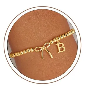 Gold beaded stretch bracelet with bow and letter B charm, stylish fashion jewelry for women.