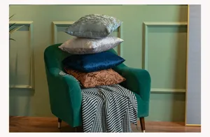 Detail shot of luxurious velvet throw pillow cases stacked on a stylish green accent chair.