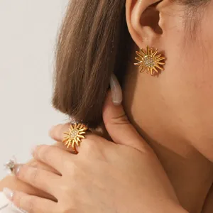 Detailed view of gold sun-shaped stainless steel earrings and matching ring with crystal pave.
