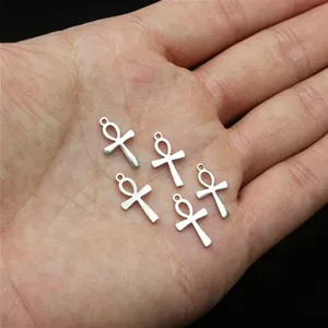 Gros plan de petits pendentifs croix ankh en acier sur la main pour la fabrication de bijoux.