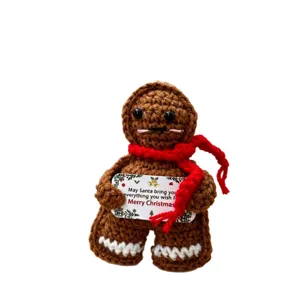 Handmade crochet gingerbread man doll with red scarf and Christmas card, perfect holiday gift.