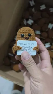 Handmade crochet potato doll holding a positive message card, cute knitted desk decor.