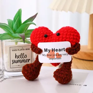 Close-up detail of a cute handmade crochet red heart doll holding a sweet message card indoors.