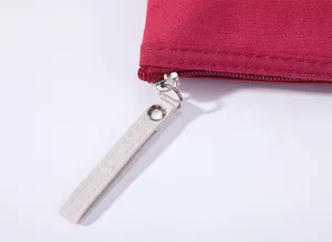 Close-up detail of red canvas zipper pouch with white strap and metal pull. Zipper detail.