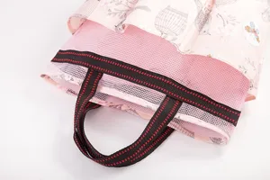 Detailed shot of pink mesh toiletry bag, featuring sturdy handles and lovely floral pattern fabric.