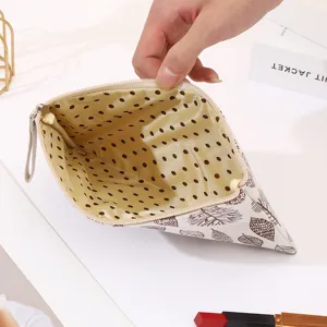 Canvas makeup pouch detail showing brown leaf pattern exterior and gold dot satin lining.