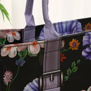 Vista detallada de bolsa tote de polipropileno tejido negro con flores y asas violetas.