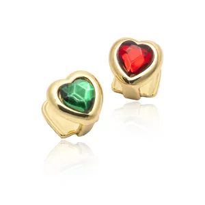 Close-up detail of gold hip-hop grillz teeth with red and green heart crystal stones.