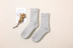 Nahaufnahme von kuscheligen grauen Winter-Wollsocken auf strukturiertem Stoffhintergrund.