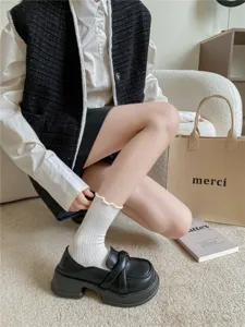 Weisse Wadensocken mit zarter Rueschenspitze, kombiniert mit klassischen schwarzen Loafern.