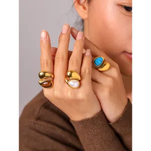 Close-up of stylish teardrop metal rings with colorful natural stones on model's hand.