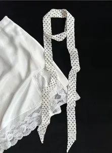 Vista di dettaglio di una sciarpa chic a pois e gonna in satin con pizzo bianco.