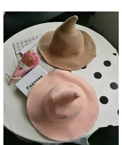 Primo piano di cappelli da strega in maglia kaki e rosa, esposti su un tavolo bianco decorato.