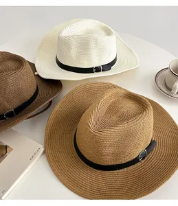 Close-up detail view of woven straw sun hat with leather belt and metal buckle, beach style.