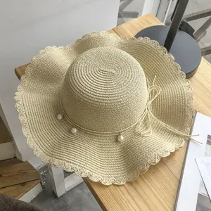 Detail view of the beige straw sun hat with wavy brim, pearl details and elegant bow tie.