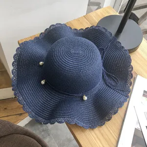 Detail shot of navy straw sun hat with wavy brim, delicate pearl decor and string bow for summer beach.