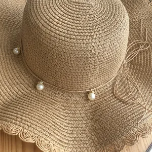 Detail view of woven straw sun hat with pearl charms and side bow for summer beach vacation.