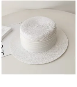 Detail view of white flat-top straw hat with ribbon, perfect for summer sun protection.