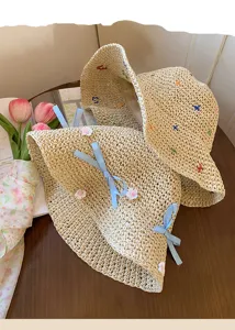 Women's hollow woven straw hat with blue bow and floral decor for beach sun protection.