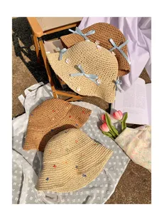 Close-up detail of straw sun hat with blue ribbon bow and delicate floral embroidery.
