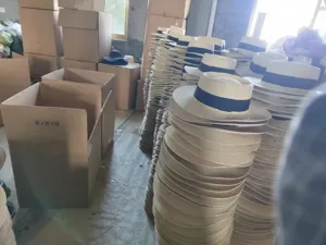 Detailed view of wholesale straw flat top sun hats with navy blue bands stacked in warehouse.