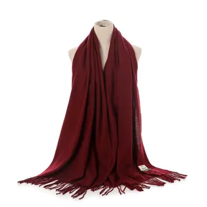 Detailed view of solid dark red cashmere-feel winter scarf for women with fringe and small label.
