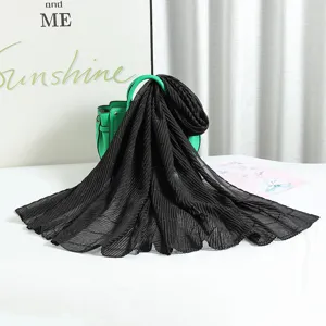 Detailed view of the black pleated shimmering scarf draped over a green handbag in studio scene.