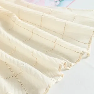 Close-up of pleated beige scarf showing delicate metallic grid texture and soft draping fabric.