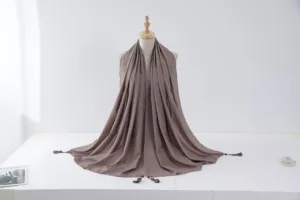 Detail view of a shimmering silver-trimmed hijab scarf with tassel beads on a mannequin stand.