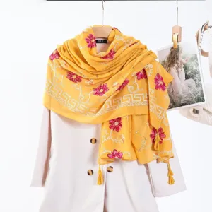 Close up detail of yellow embroidered tassel scarf showcasing intricate floral patterns and rhinestones.