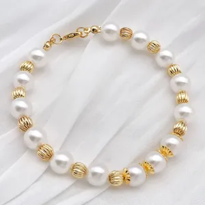Close-up detail shot of elegant white pearl and gold-tone ribbed bead bracelet accessory.