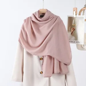 Vue détaillée de l'écharpe unie rose doux drapée élégamment sur un manteau blanc.