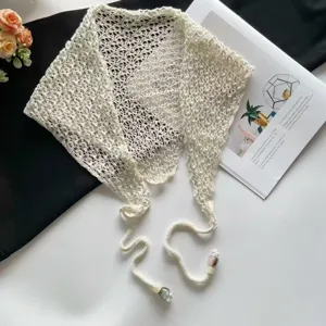 Vista detallada del pañuelo triangular de punto calado crema con cuentas y cordones.