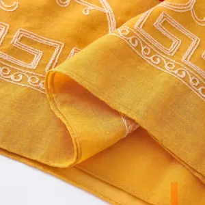 Close up detail of yellow cotton linen scarf featuring elegant white embroidered geometric pattern.