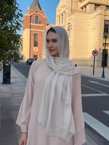 Detailed view of the solid color bubble scarf and light outerwear worn outdoors in sunlight.