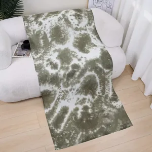 Green tie-dye gradient scarf draped on modern white sofa, showing detailed fabric texture.
