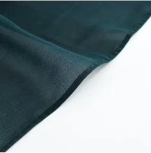Primo piano di tessuto chiffon verde scuro con dettagli di orlo arrotolato e morbido drappeggio.