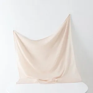 Close-up detail of pleated scarf showing fine texture and elegant drape on white wall.