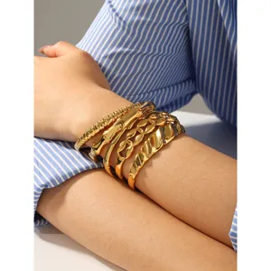 Vue de détail de plusieurs bracelets manchette irréguliers en acier inoxydable doré sur le poignet.