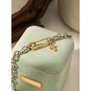 Stainless steel two-tone paperclip chain bracelet with rhinestone cross pendant detail.