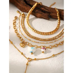 Close-up detail of layered gold stainless steel bracelets featuring heart charms and cubic zirconia.