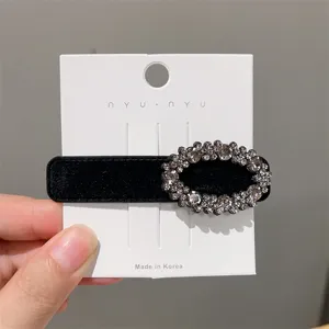 Close-up detail of black velvet hair clip with sparkling rhinestone oval charm on white card.