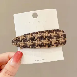 Close-up view of the brown houndstooth hair clip detail, featuring tweed fabric and secure metal clip.