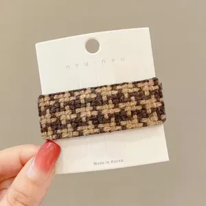 Close-up detail of a brown houndstooth hair clip with soft wool texture and display card.