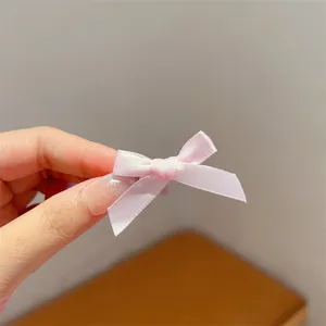 Close-up detail of a sweet pink satin ribbon bow hair clip, showing texture and small size.