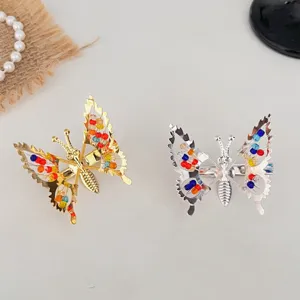 Détail en gros plan de pinces à cheveux papillon avec ailes en métal ajouré et perles colorées.