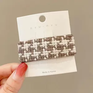 Close-up detail of a brown and white tweed hair clip on a white card, elegant winter hair accessory.