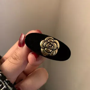 Zwarte fluwelen haarspeld met gouden camelia bloem detail, close-up van retro design.